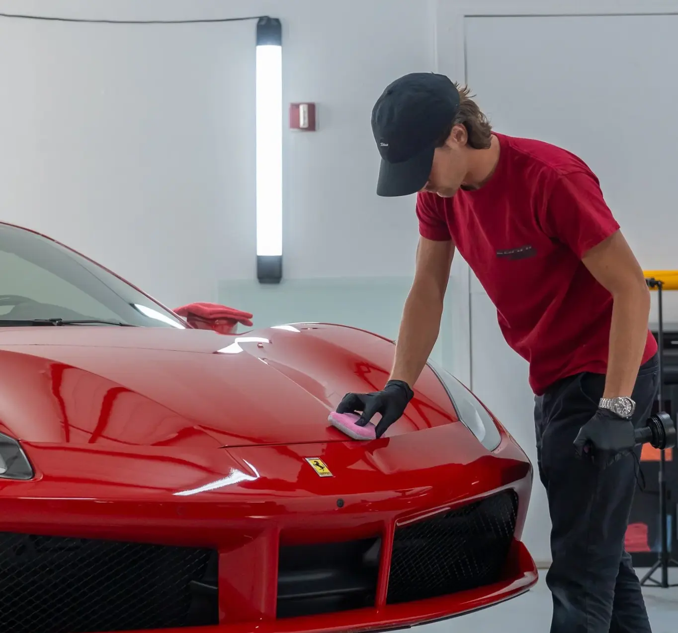 Technician wiping down the hood of a red Ferrari